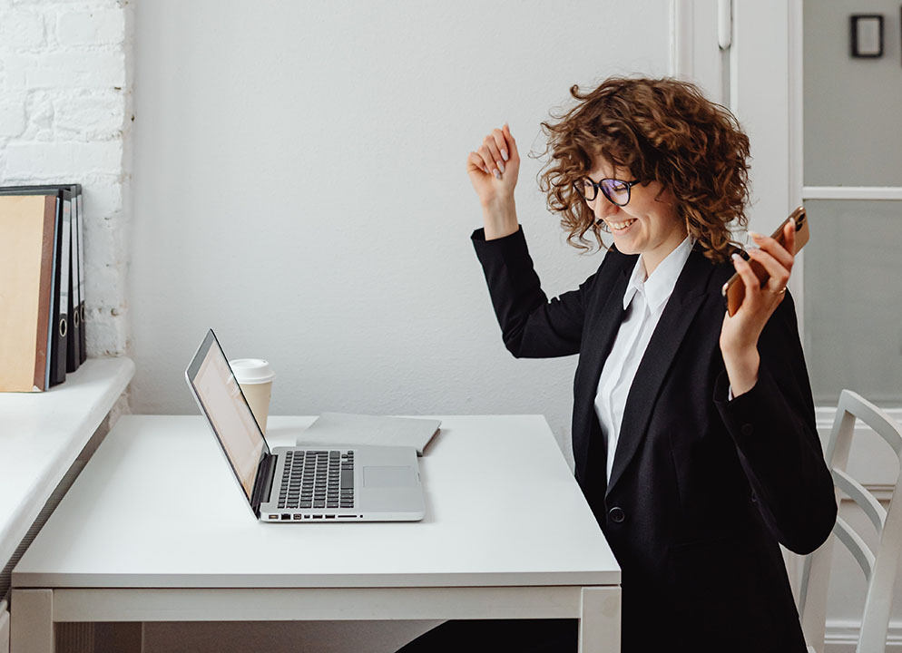 How to Improve Internet Speed & Performance Woman in business suit with hands up in excitement over internet speed. Viewing computer with phone in her hand