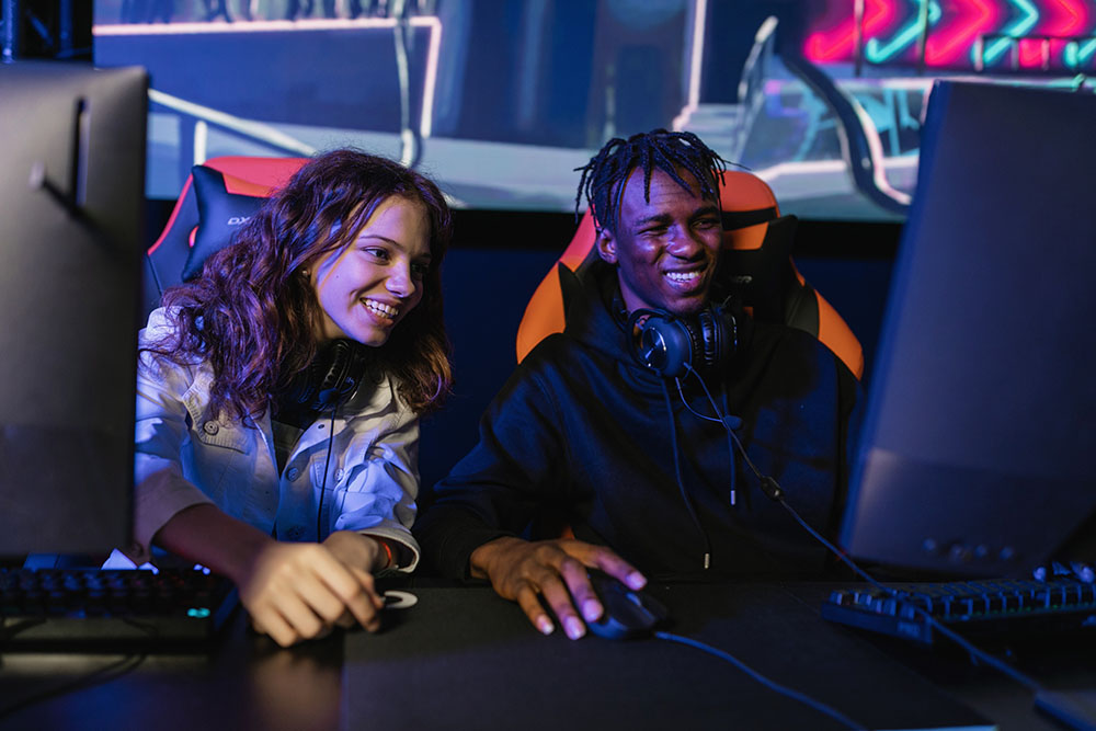Improve Internet Gaming Speed Guy and girl sitting at gaming PCs and smiling at video game event.
