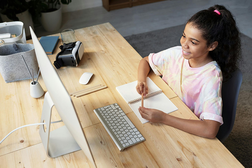Home school girl working on school lesson looking at her computer and taking notes.